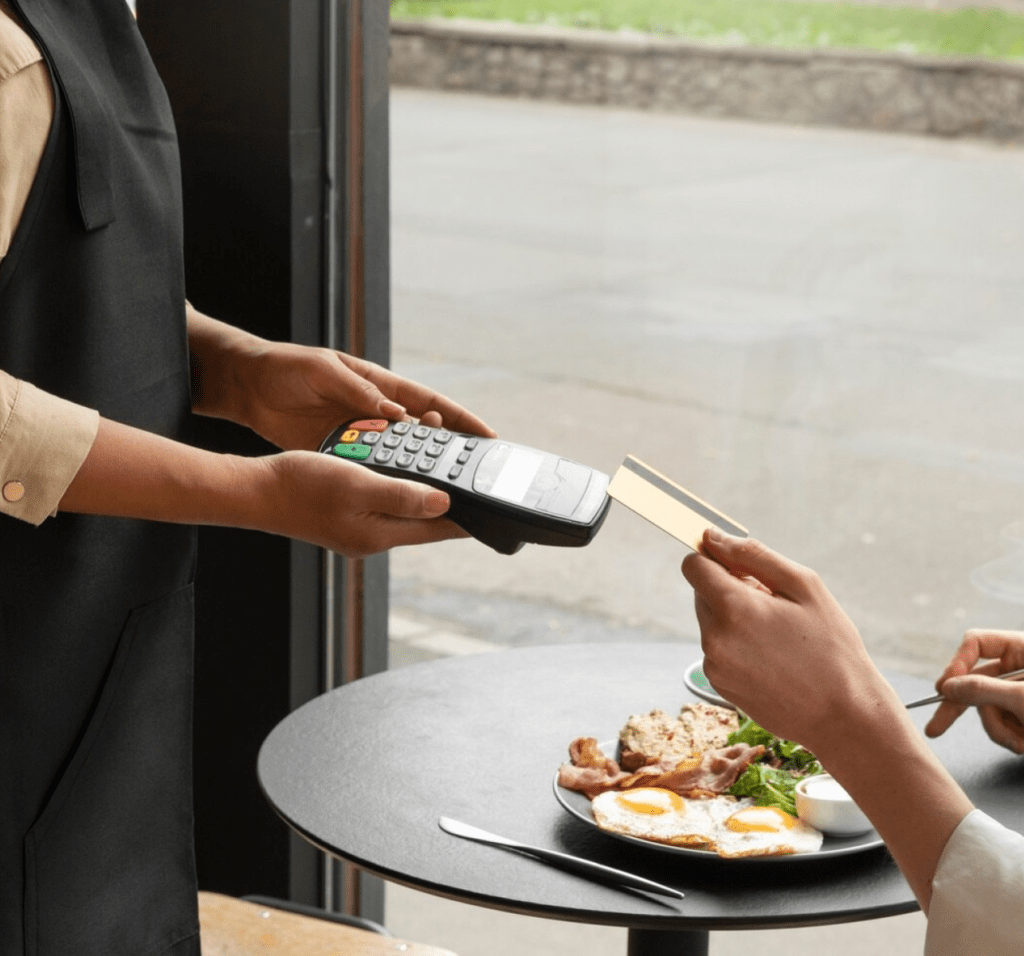 Cliente realiza pagamento com cartão em uma maquininha, após refeição em restaurante, simbolizando praticidade no atendimento.